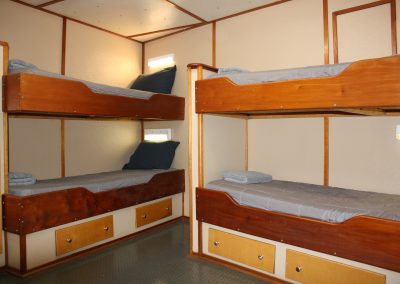 Interior view of a crew berthing cabin on the R/V Peter M Mahoney featuring two sets of wooden bunk beds with built-in storage drawers.