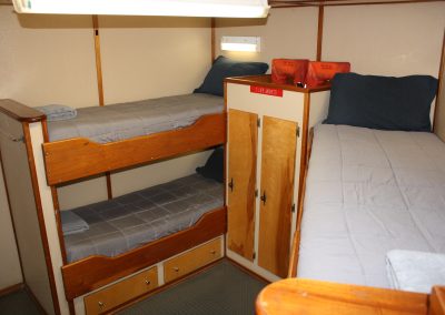 Interior view of a crew berthing cabin on the R/V Peter M Mahoney featuring wooden bunk beds, a storage wardrobe, and designated life jacket storage.