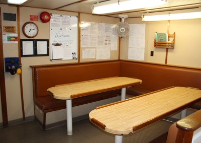 Interior view of the crew dining and briefing area inside the R/V Peter M Mahoney, featuring booth seating, tables, and safety bulletin boards.